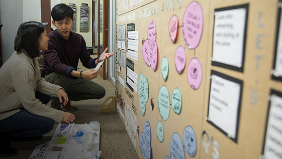 Two EDI students conversing in front of a board in a classroom.