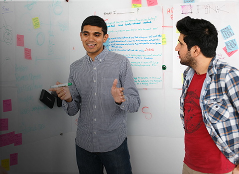 Two MMM students talk in front of notes on a board.